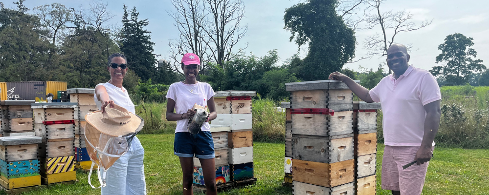 Three people standing with stacks of wooden beehives in an outdoor setting.