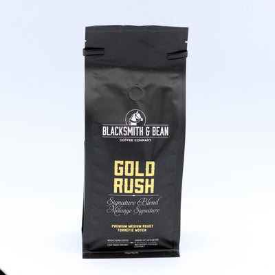Black coffee bag labeled 'Gold Rush' from Blacksmith & Bean Coffee Company on a light gray background